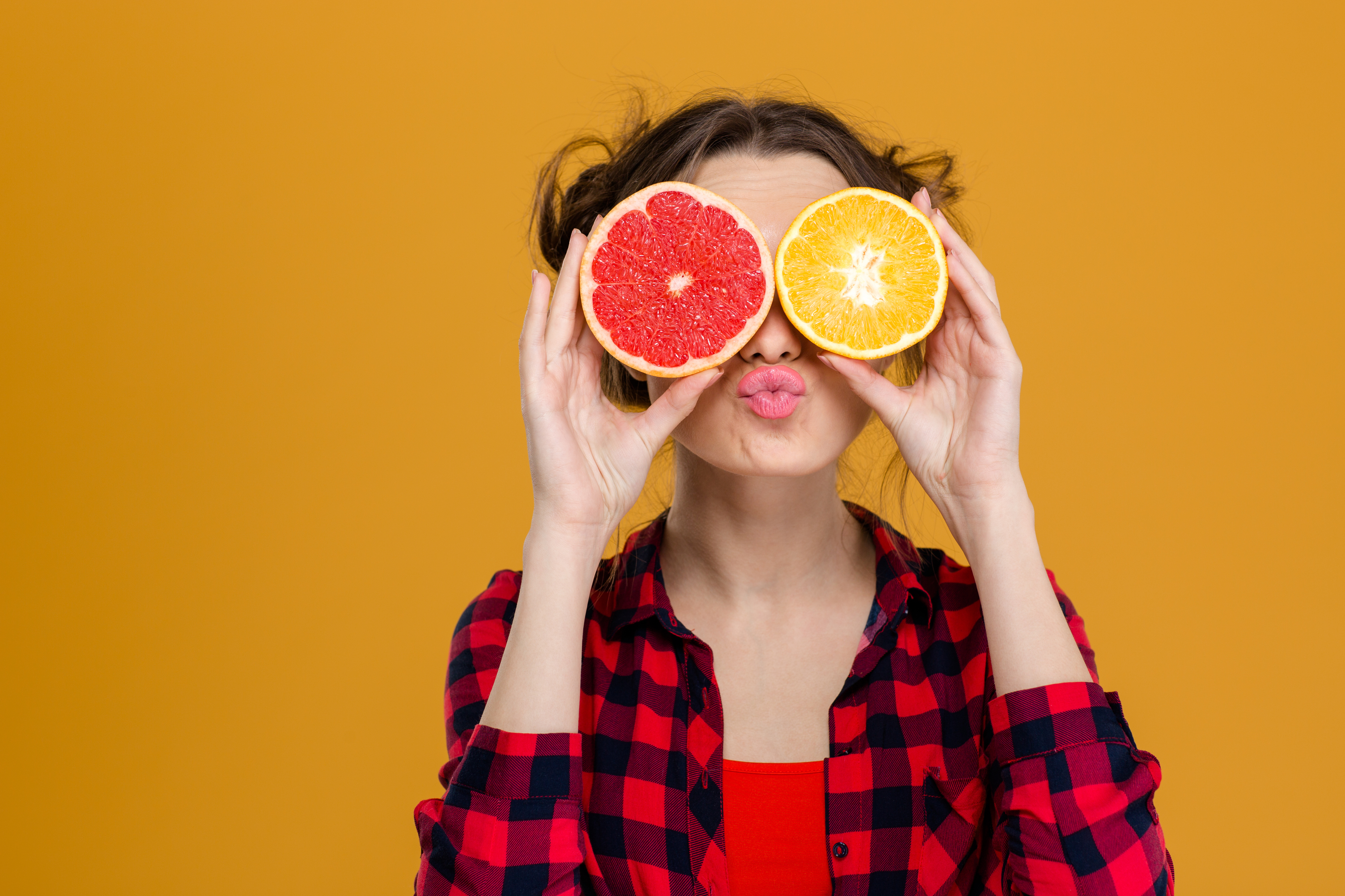 Funny playful young woman in checkered shirt holding halves of citrus 